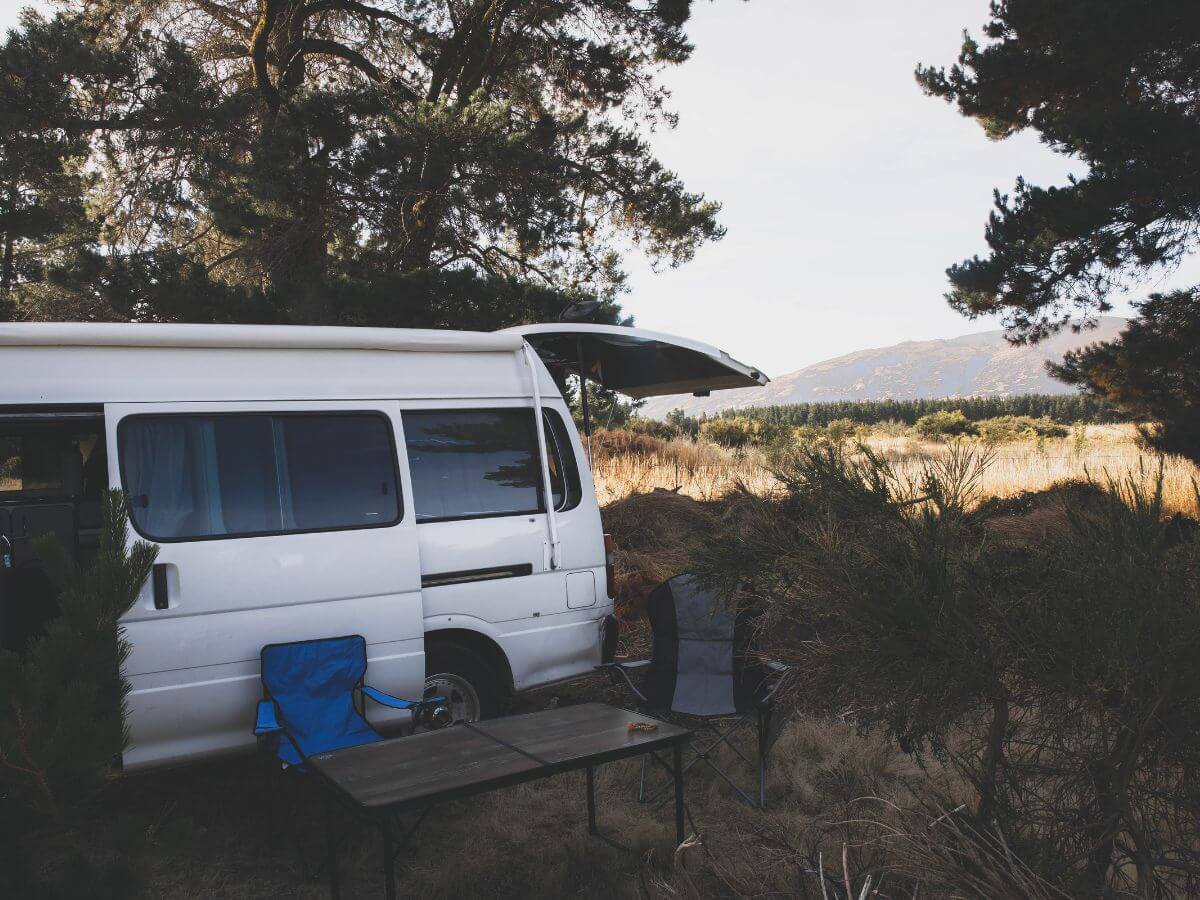 A white van parked up in a secluded camp ground overlooking a hill